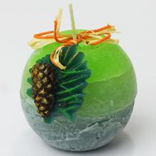 Ovocná sviečka so zelenou a šedou farbou, ozdobená šiškou a listom.