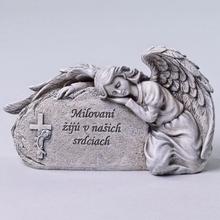 Smutný anjel ležiaci na kameni s nápisom Milovani žijú v našich srdciach.