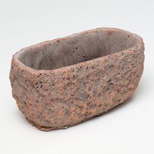 Šedý oválny cementový obal s medeným detailom.