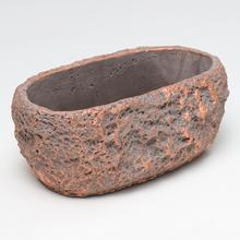 Šedý oválny cementový obal s medenými detailmi.