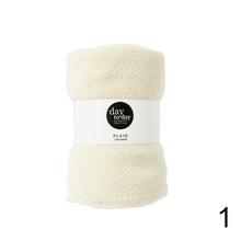 Pléd v krémovej farbe, rozložený a zrolovaný.
