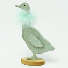 Drevená huska na podstavci s pierkom modrej farby.