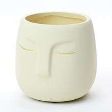 Biely kvetináč s otvorom v tvare tváre.